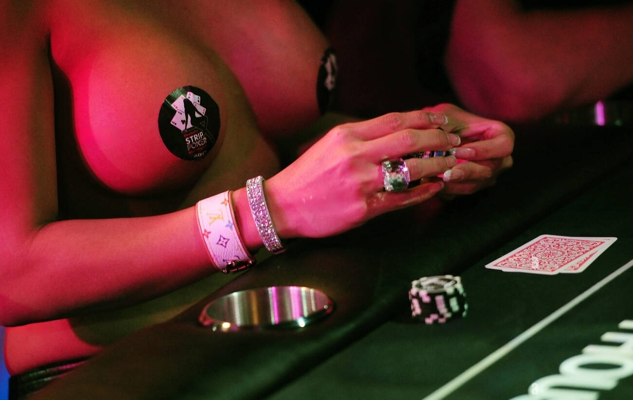 A close-up of a player's hands holding naked poker chips and cards, with poker chips strategically placed, in a dramatic, neon-lit environment.